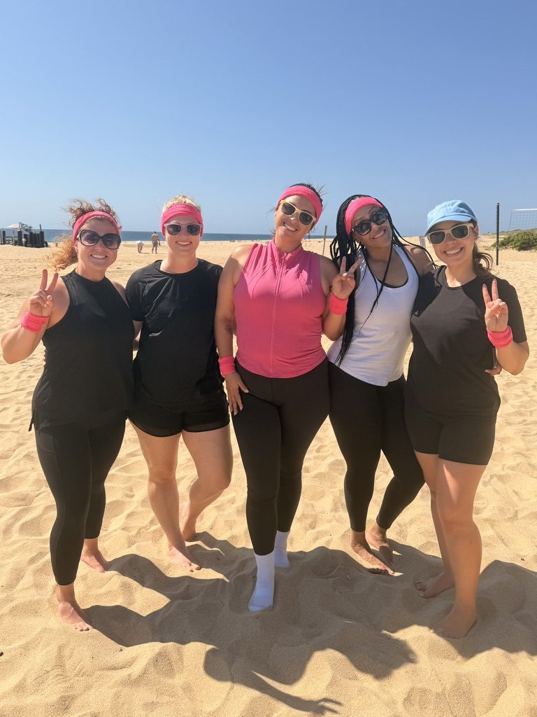 Carol and four teammates in pink headbands on a beach volleyball court